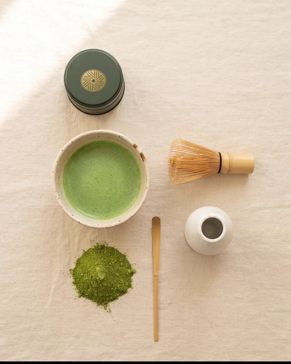 Indholdet i matcha-sættet set oppefra: dåse med guldsegl, skål med matcha, bambuspisker, piskeholder, bambusske og matcha pulver